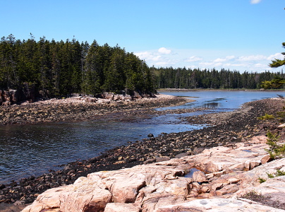 [Water flows from lower left to pool-like setting in middle right. Trees seen on far shore with a large rocky expanse seen on near shore. Lots of stones along the water's edge.]